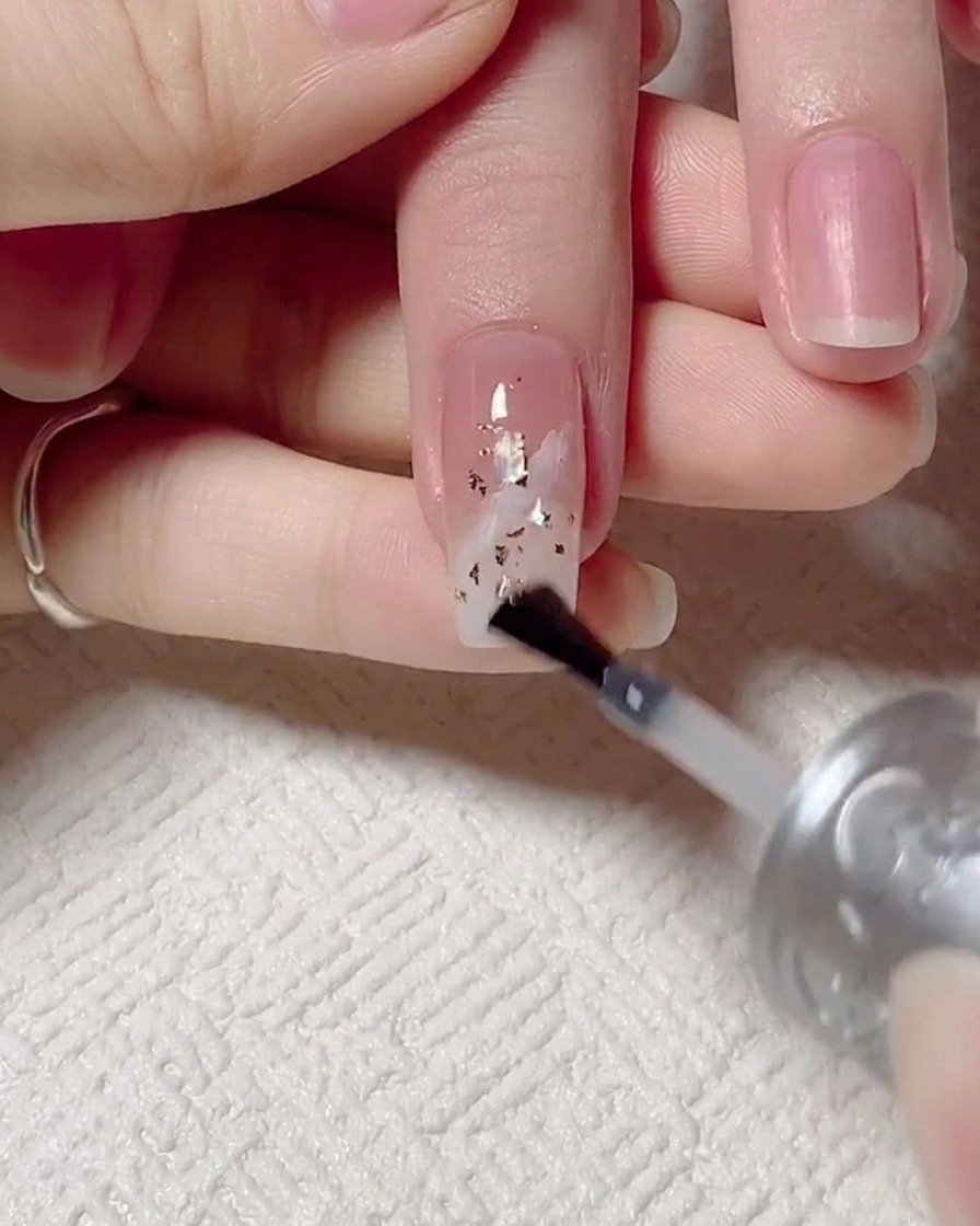 Un pennello che applica un top coat lucido finale sopra lunghia decorata, seguita dallunghia posta sotto una lampada UV.