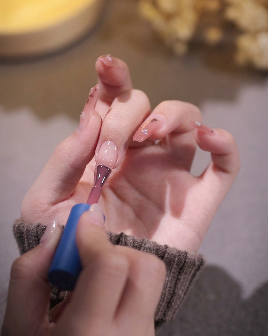 Un pennello per unghie che applica uno smalto gel rosa traslucido su ununghia preparata.