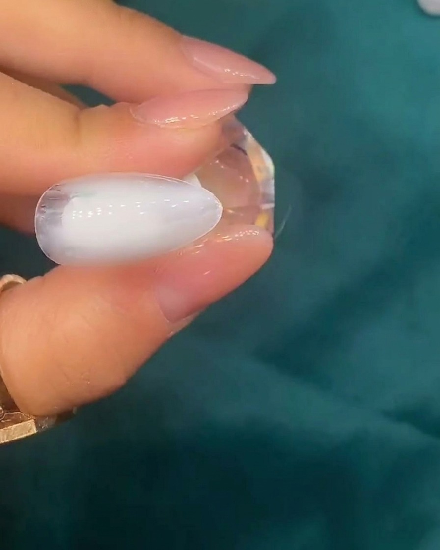 Pinzette che posizionano piccoli frammenti di conchiglia iridescente sulla superficie di ununghia con base bianca.