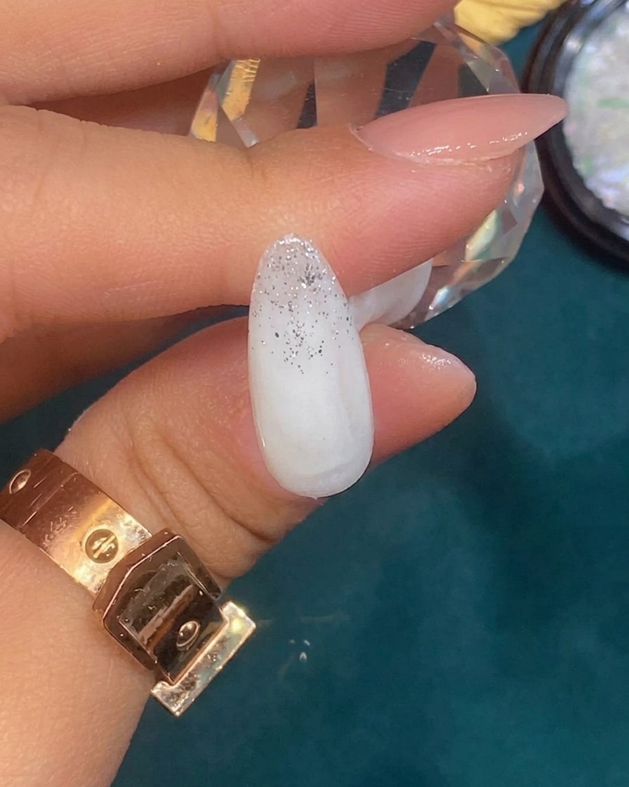 Pinzette che posizionano un piccolo pezzo irregolare di foglia argento su ununghia con gradient glitterato.