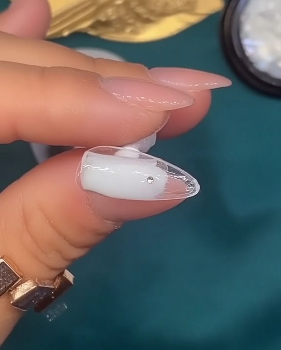 Un pennello applica uno smalto gel bianco lattiginoso traslucido su ununghia di forma naturale.