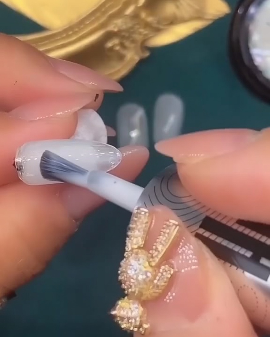Un pennello per unghie applica uno strato di smalto gel bianco traslucido sulla quinta unghia.
