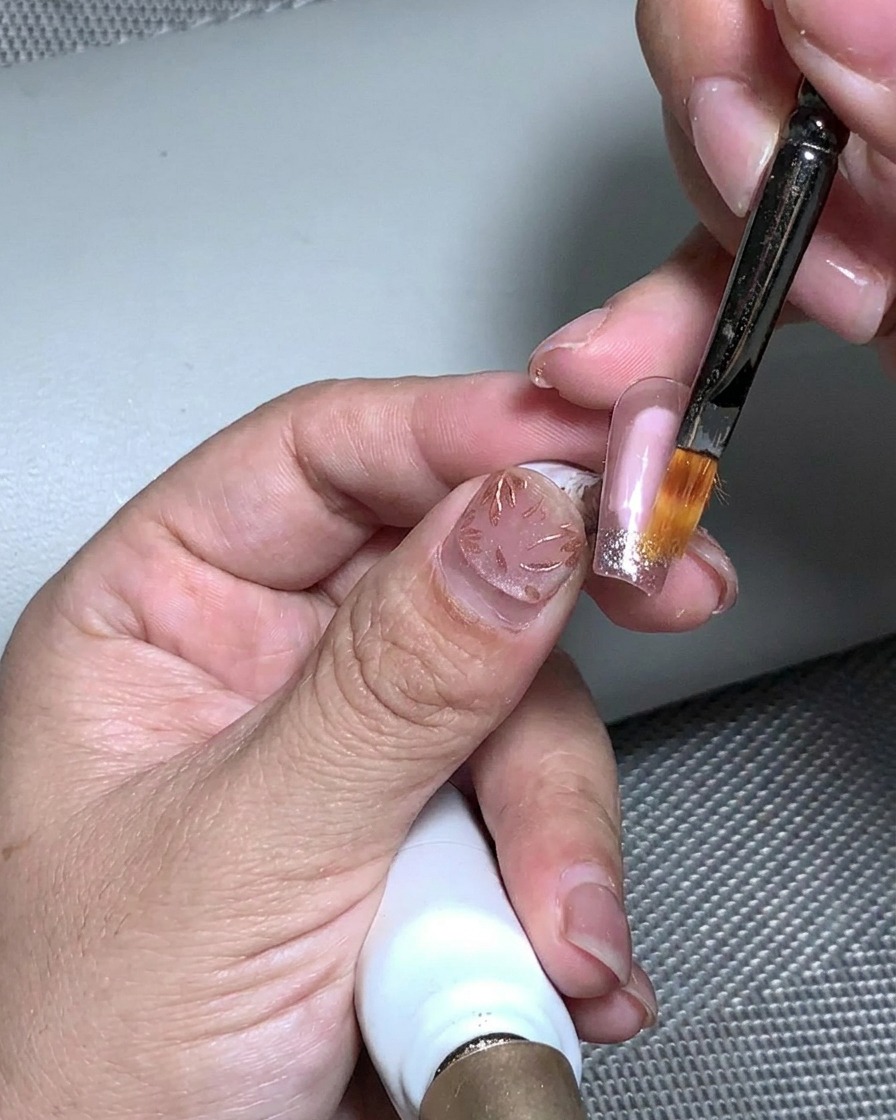 Un pennello che applica gel strutturale trasparente sulla superficie testurizzata di foglia oro e glitter.