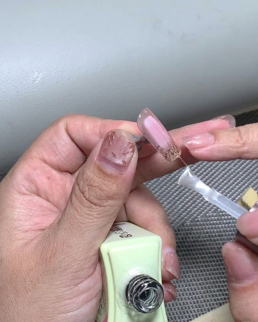 Un pennello che applica uno strato finale di top coat trasparente su un design French completato.