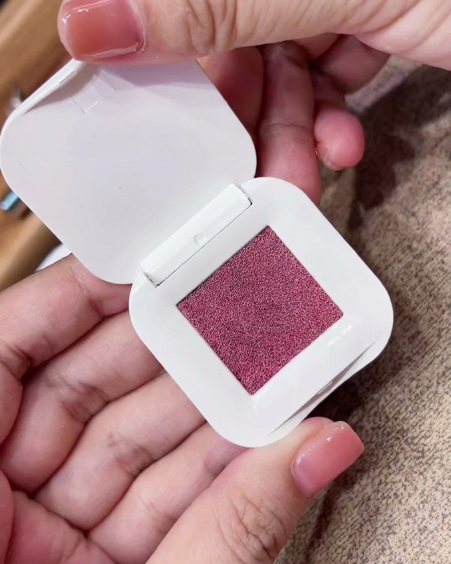 Primo piano di una spugnetta per makeup triangolare che preme su una cialda di pigmento rosa-viola.