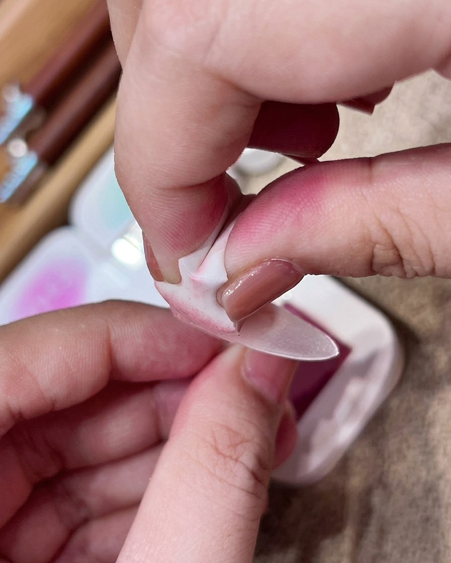 Una mano usa una spugnetta per picchiettare delicatamente il pigmento rosa al centro di ununghia nude opaca.