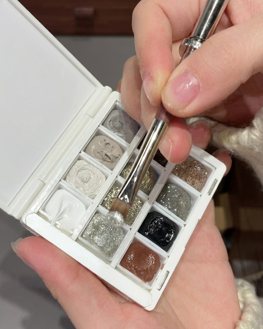 Un pennello che miscela gel glitter argento fine con paillettes argento più grandi su una tavolozza bianca.