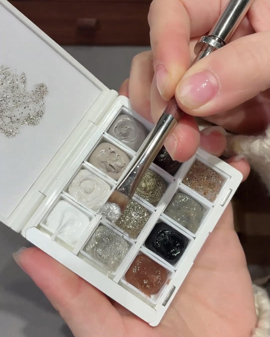Un pennello che applica un mix di glitter e paillettes argento sulla base di ununghia naturale.