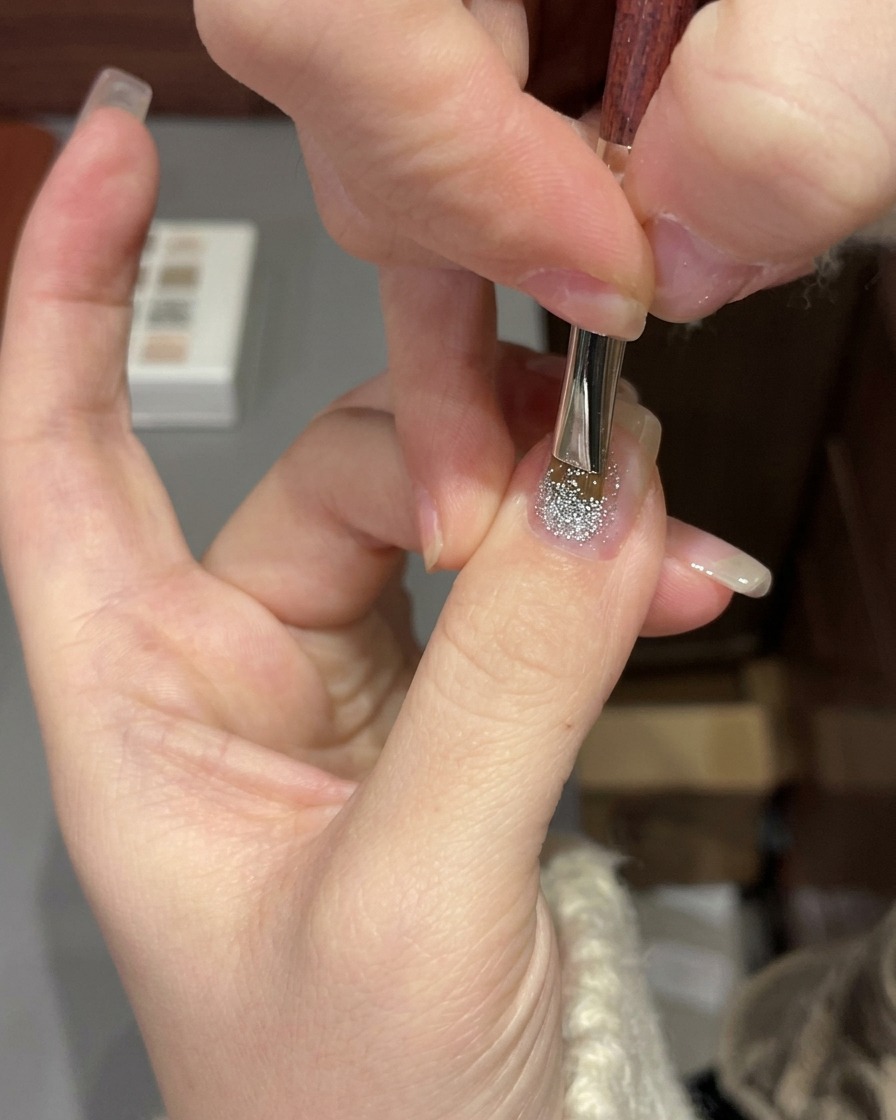 Una mano posizionata sotto una lampada UV/LED professionale per polimerizzare la manicure glitter gel.