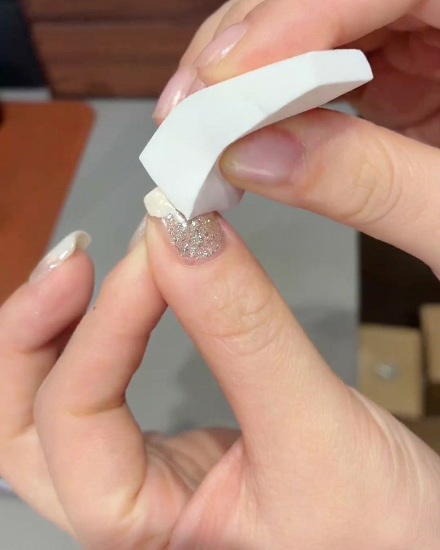 Primo piano di una spugnetta per makeup che tampona gel bianco latte sulla punta di ununghia per formare una sfumatura morbida.