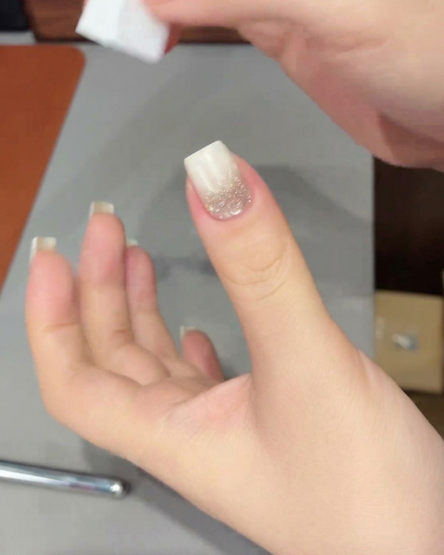 Una mano con punta sfumata bianca posizionata sotto una lampada UV/LED per polimerizzare il gel appena applicato.