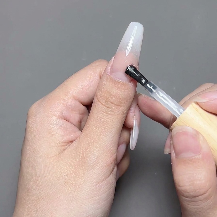 Un pennello stende un top coat in gel trasparente e lucido su un design per unghie finito.