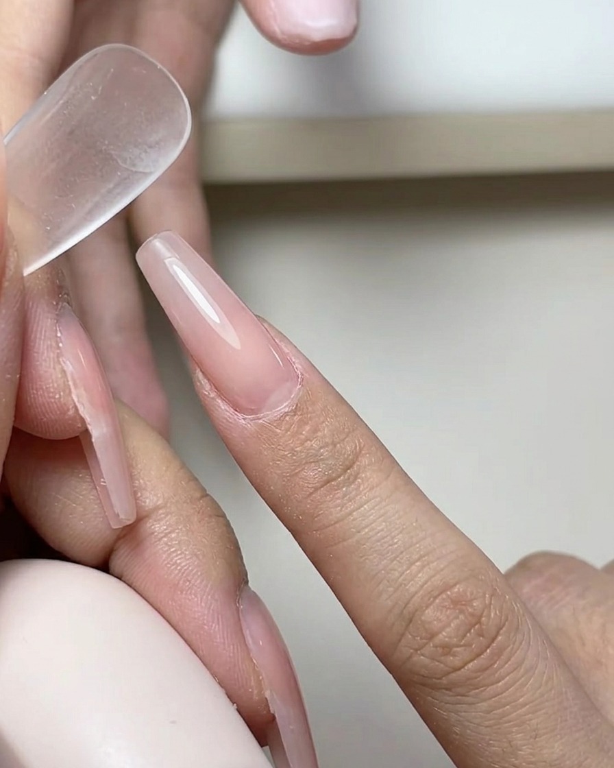 Un pennello che applica uno strato sottile e trasparente di base gel su ununghia naturale.