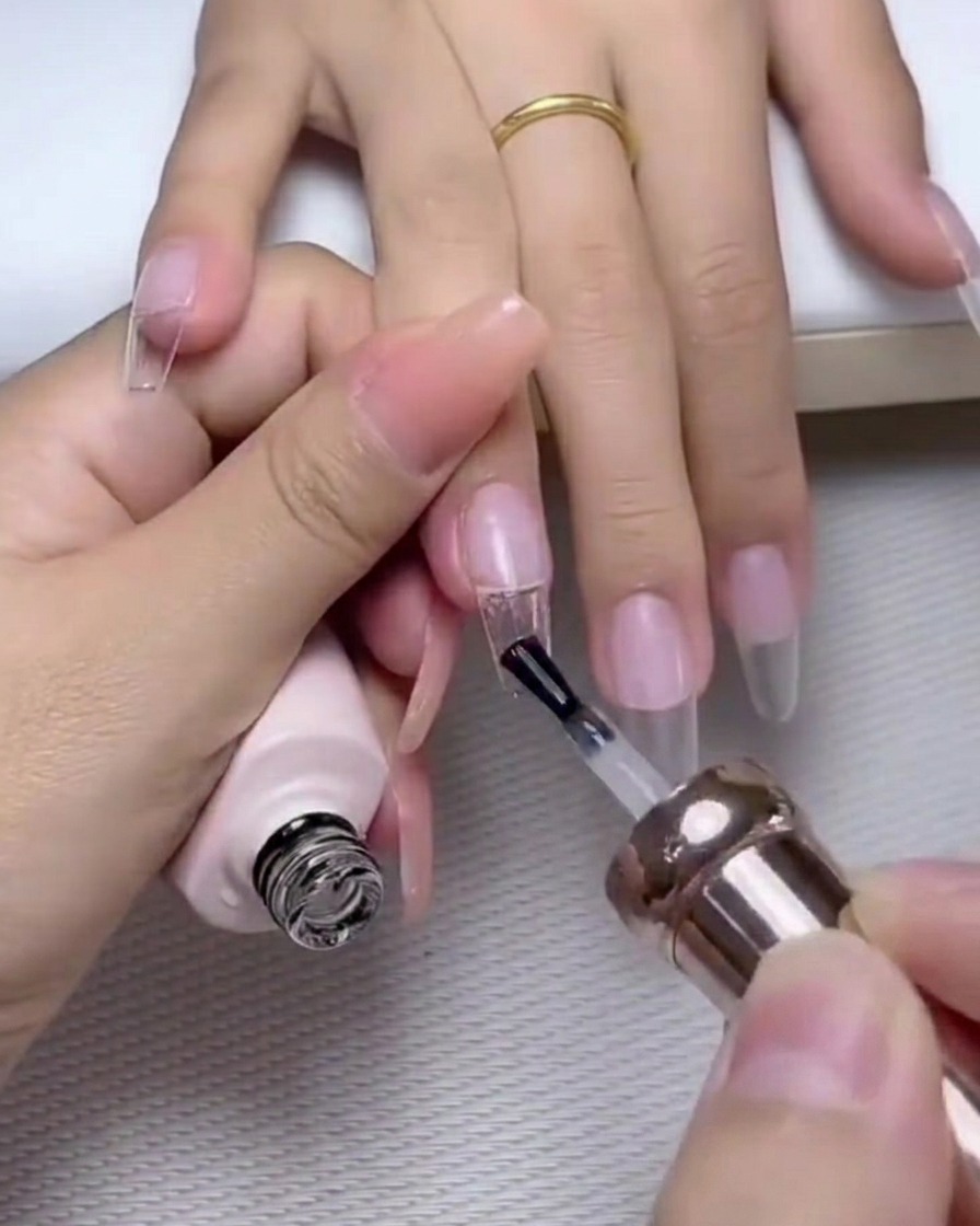 Un pennello che applica uno strato di top coat lucido sopra ununghia decorata con perle e strass.