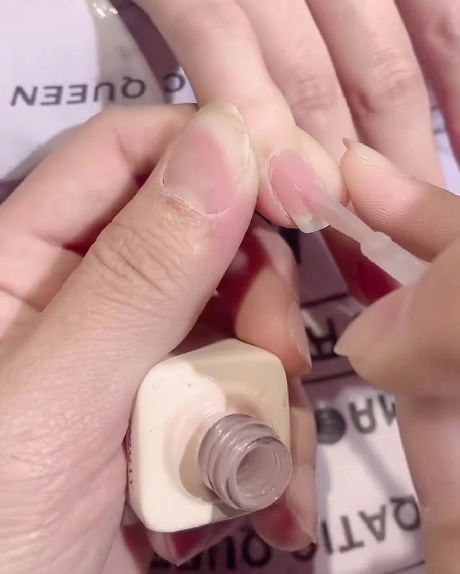 Un pennello che applica un sottile strato uniforme di base coat nude trasparente su ununghia.