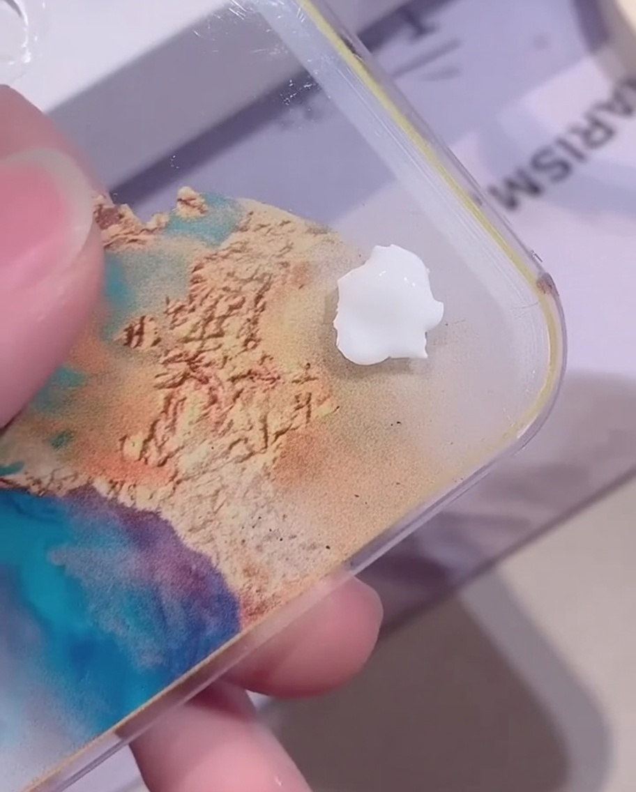Una piccola goccia di gel colorato bianco opaco su una tavolozza di miscelazione acrilica trasparente sopra uno sfondo colorato.