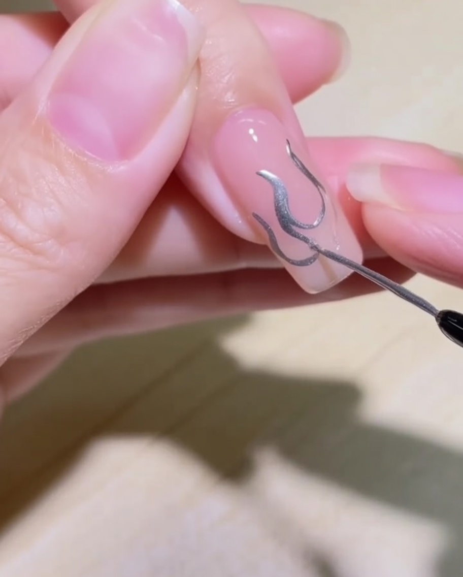 Un primo piano che mostra il design a fiamma sullunghia riempito con gel metallizzato argentato.