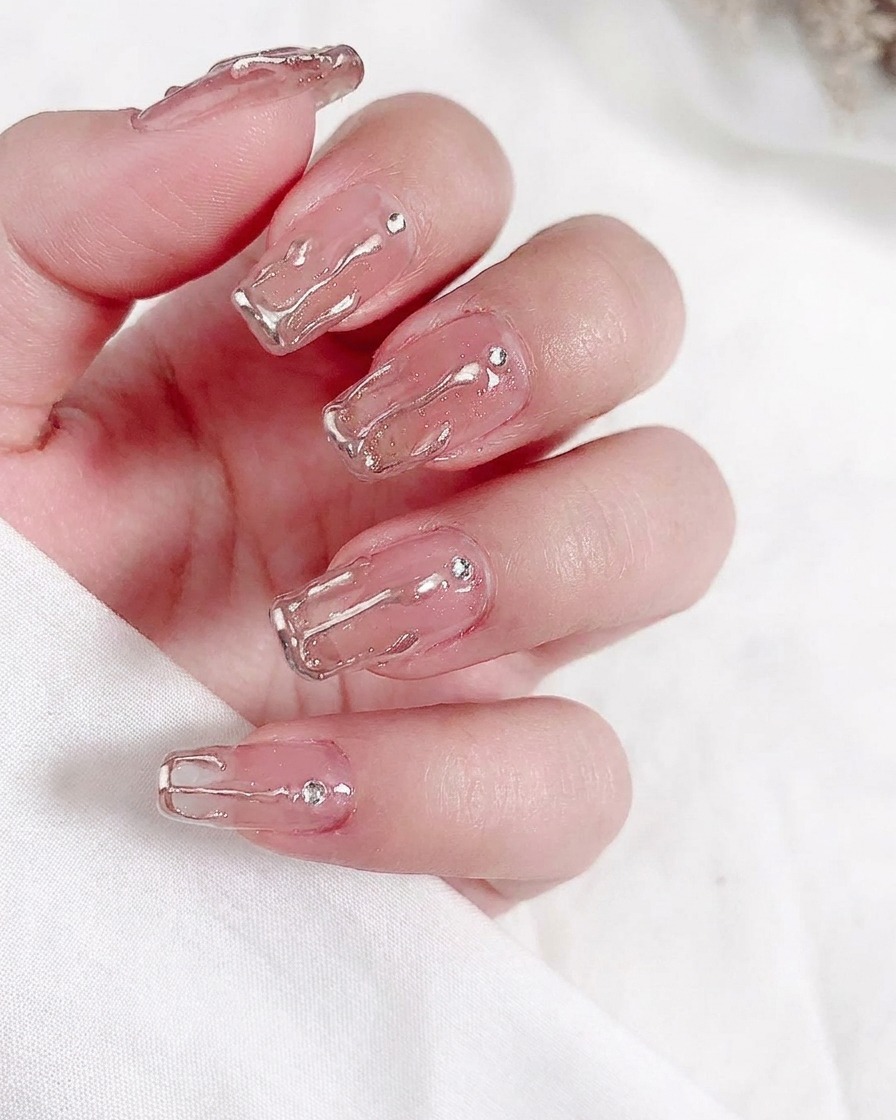 Un primo piano di un pennello che applica uno strato di smalto gel nude traslucido su ununghia naturale.
