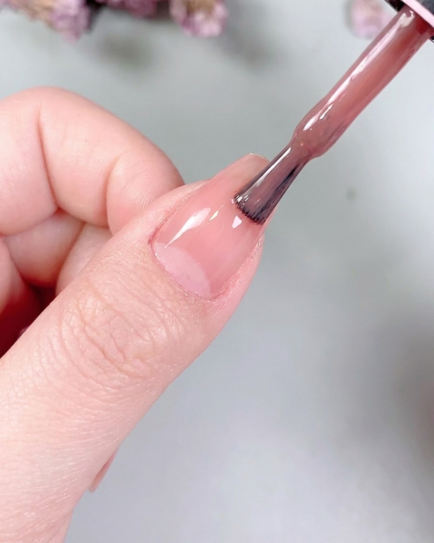 Un piccolo pennello piatto per gel che distribuisce delicatamente il colore nude sulla superficie dellunghia.