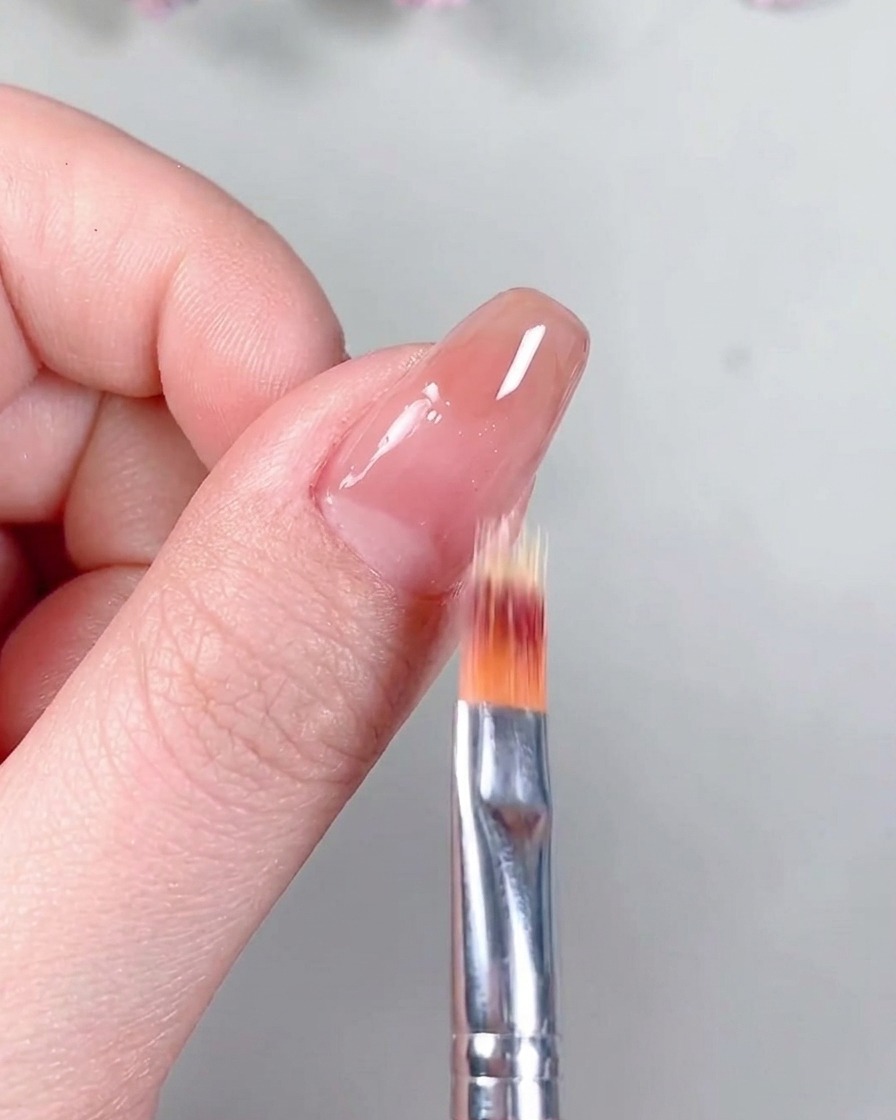 Un pennello che applica un top coat trasparente con finitura opaca sopra la base gel nude polimerizzata.