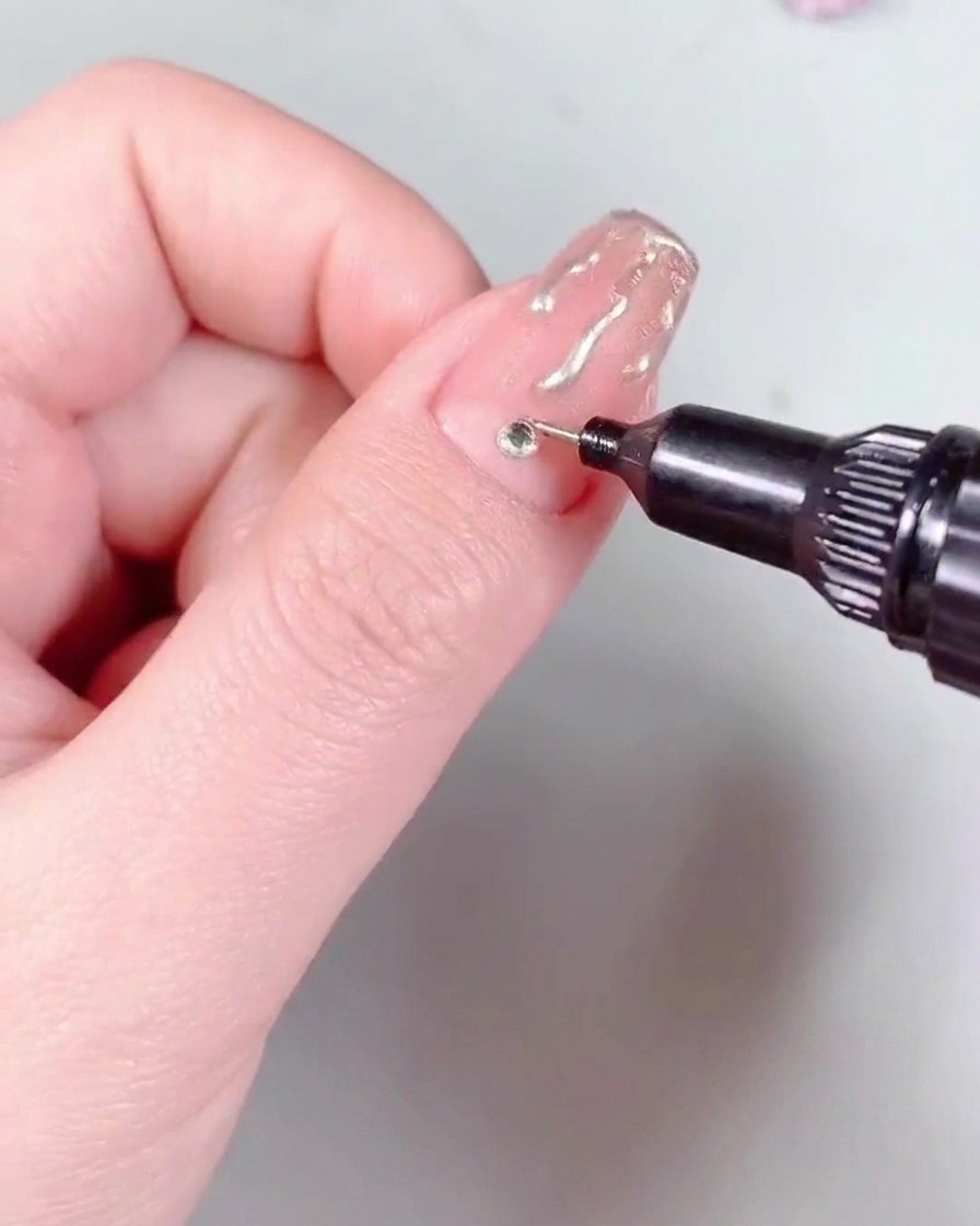 Un pennello per nail art che applica uno strato di top coat protettivo lucido sopra ununghia rifinita con nail art a fiamma e uno strass.