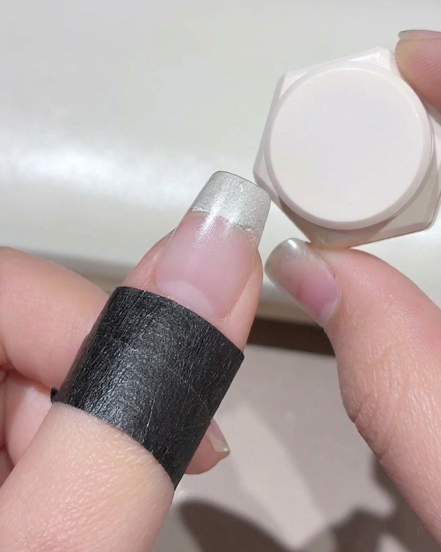 Dito con protezione nera intorno alla pelle, mostrando gel bianco latte applicato sulla punta dellunghia.