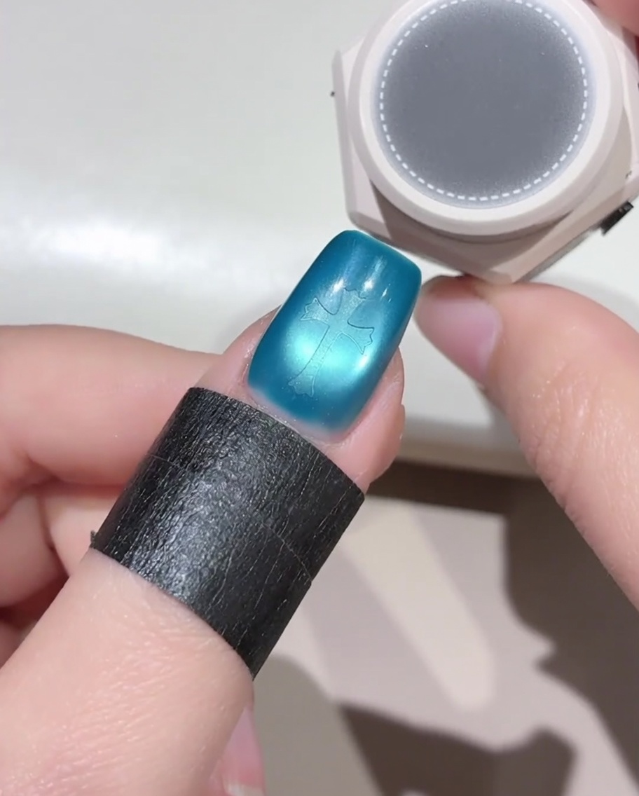 Spugnetta rotonda sopra lunghia blu con stencil a croce, pronta per applicare il gel nero.