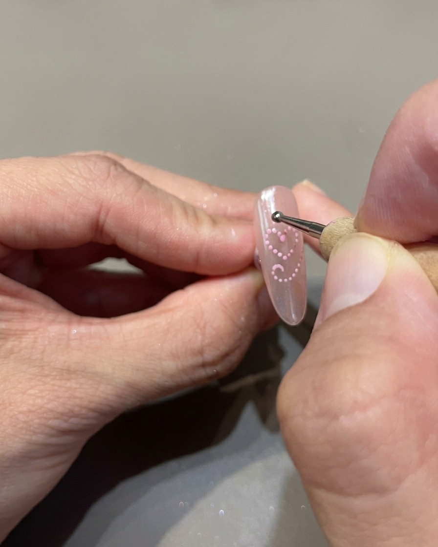 Un dotting tool posiziona piccoli punti uniformi di gel cat-eye rosa per delineare un cuore sullunghia.