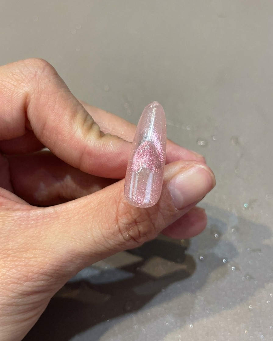 Primo piano di ununghia rosa con un design a cuore cat-eye, mentre un magnete manipola leffetto luccicante.