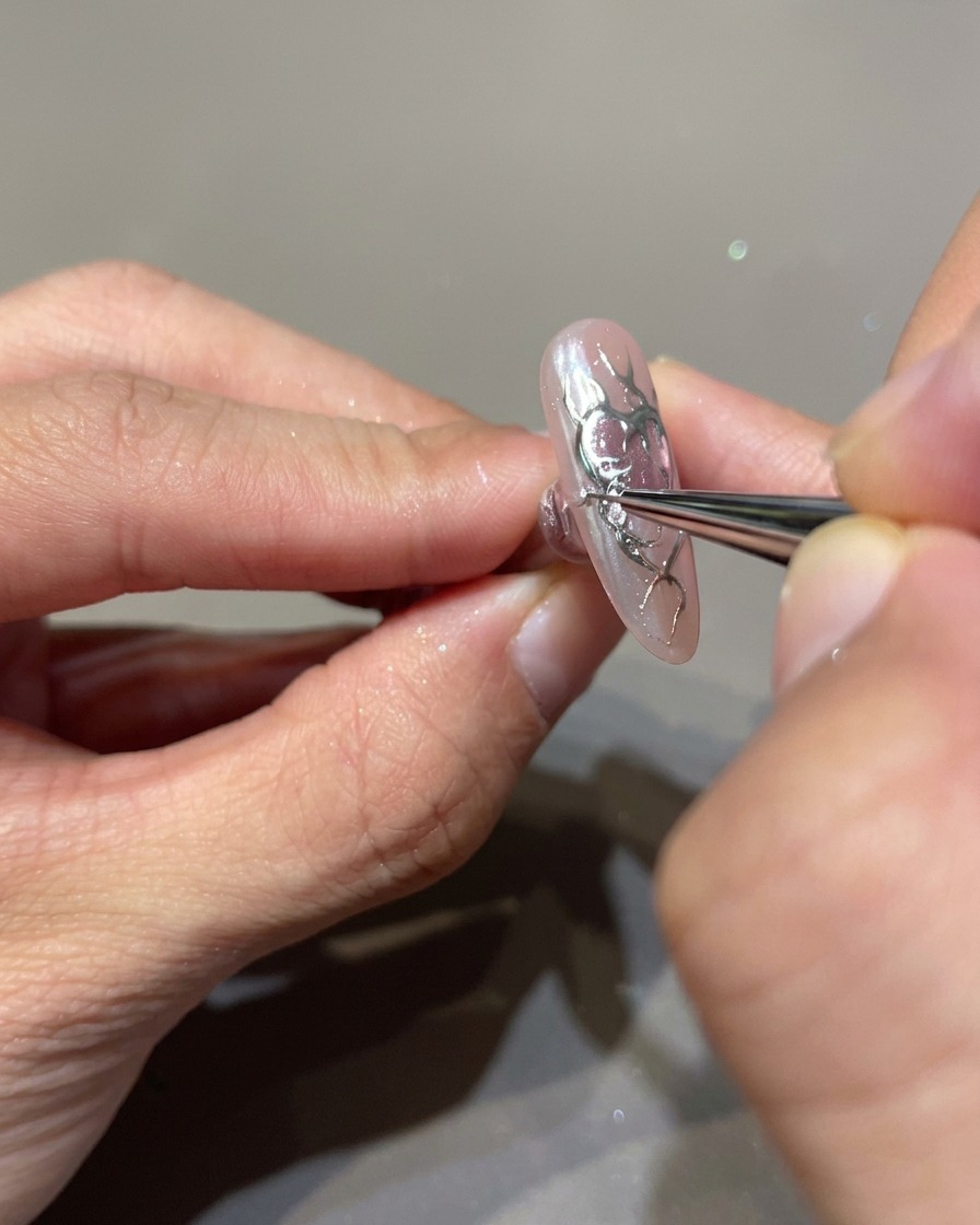 Primo piano di ununghia decorata con un pennello sottile che applica gel builder 3D trasparente sopra le fiamme nere.