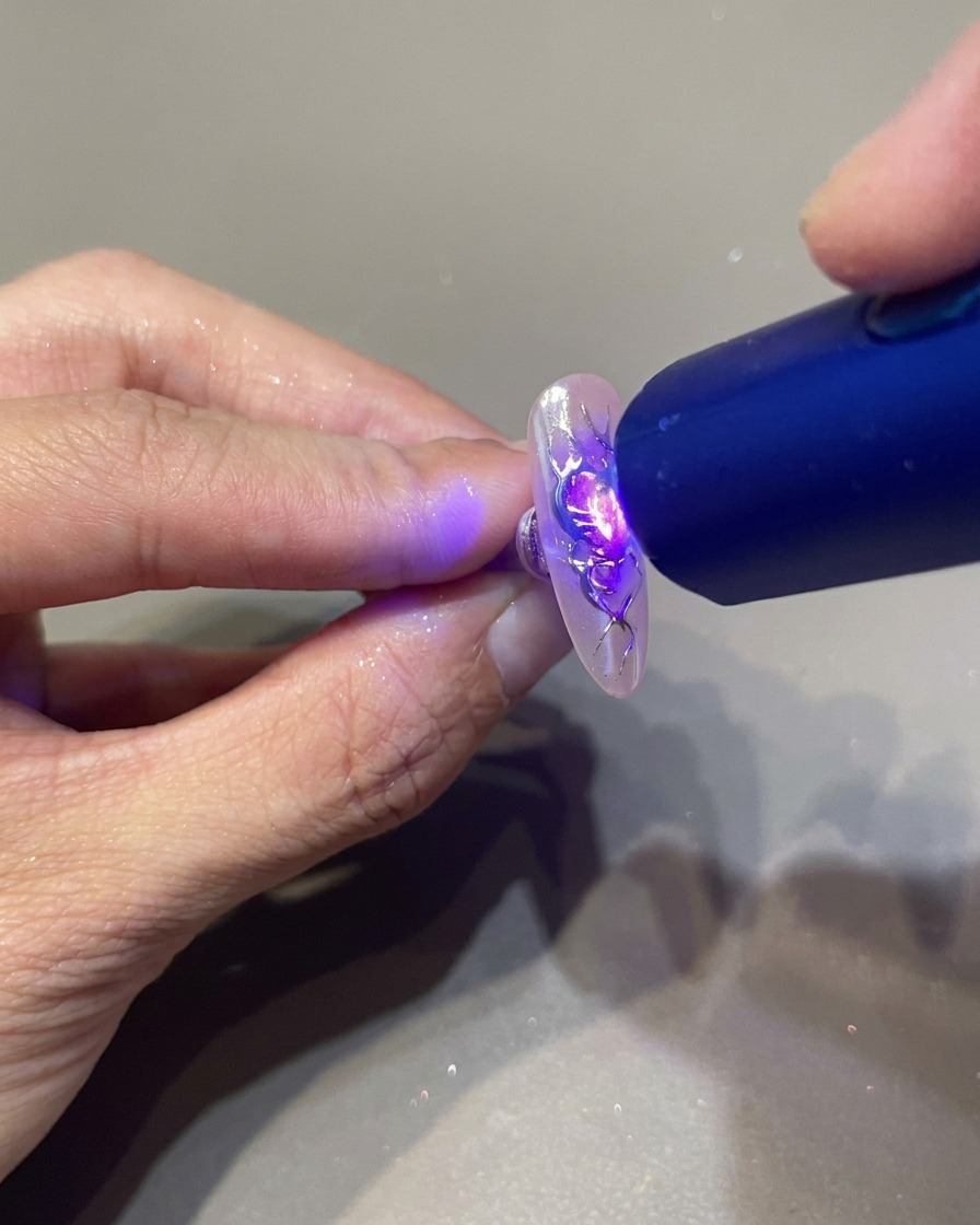 Una lampada UV portatile sopra ununghia per fissare i dettagli in gel 3D su un design a cuore con fiamme.