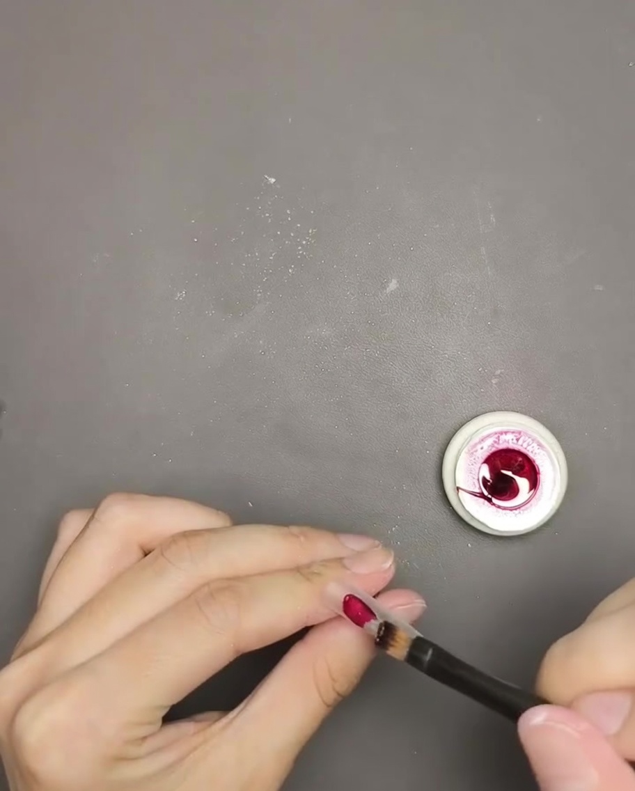 Un primo piano di un pennello che applica gel polish rosso cat eye su una tip.