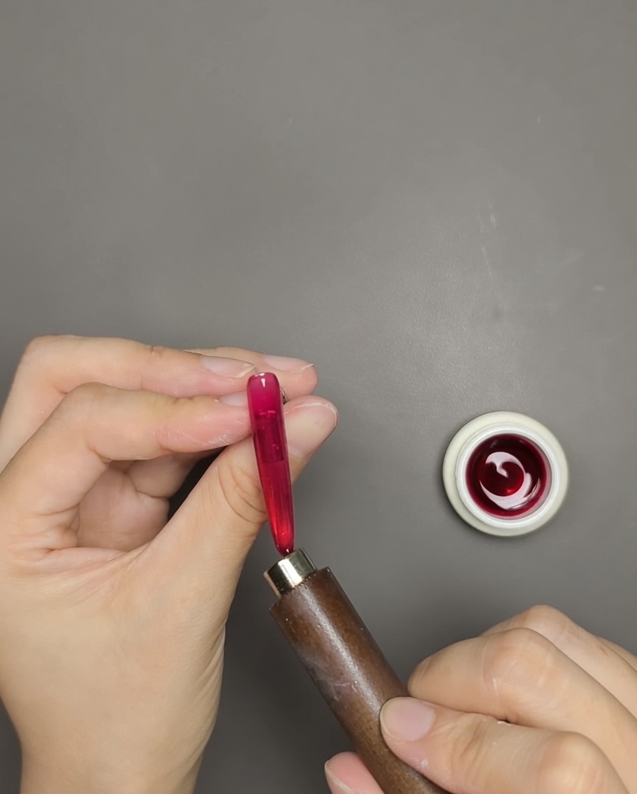 Una mano usa un magnete a barra vicino a ununghia con gel cat eye rosso per rivelare la linea scintillante magnetica.