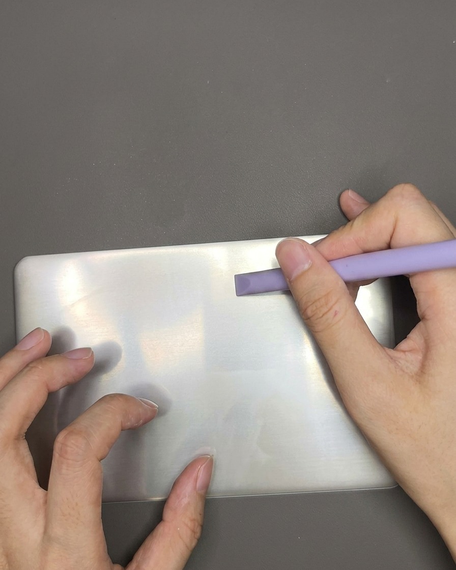 Uno strumento raschietto in plastica che scorre su una piastra per stamping in metallo per rimuovere lo smalto bianco in eccesso.