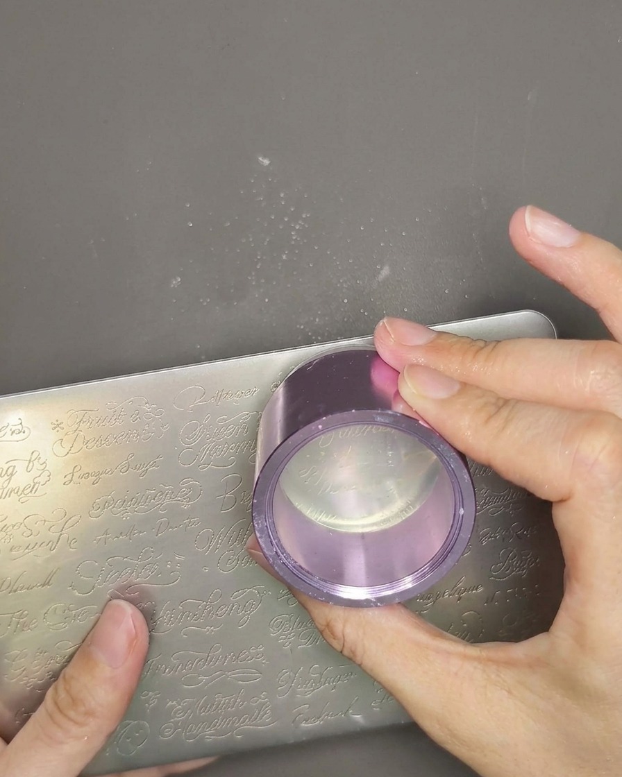 Un primo piano di una testina per stamper in gel trasparente tenuta in mano, con un sottile strato di smalto bianco applicato sopra il design precedentemente prelevato.