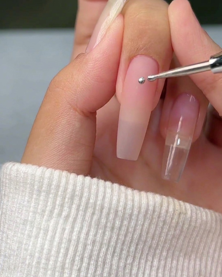 Una vista ravvicinata di uno strumento dotting che applica una singola sfera perfetta di gel metallizzato argento su una superficie pulita dellunghia naturale.