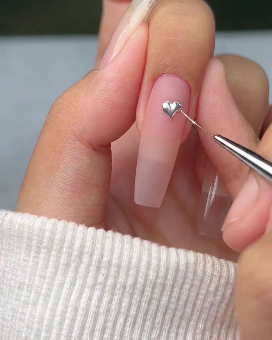 Un pennello liner sottile che tira delicatamente i bordi di un punto di gel argento per formare un cuore definito sullunghia.