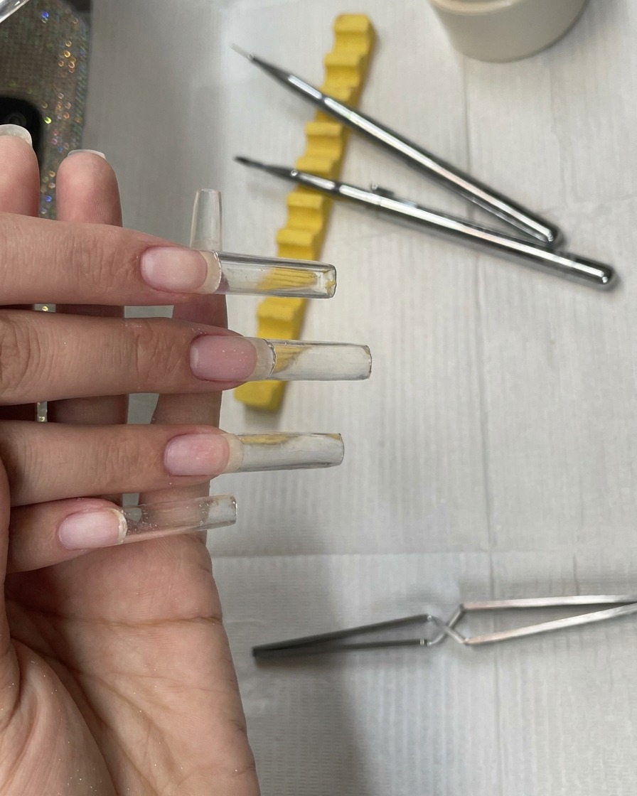 Quattro estensioni ungueali quadrate extra-lunghe in gel trasparente completamente costruite e non polimerizzate su una mano prima della fase di limatura.