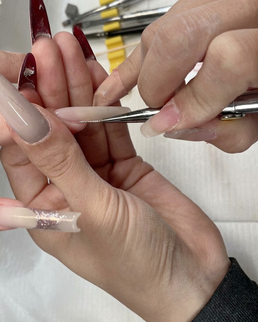 Primo piano di un pennello liner che applica glitter oro rosa attraverso il letto ungueale.