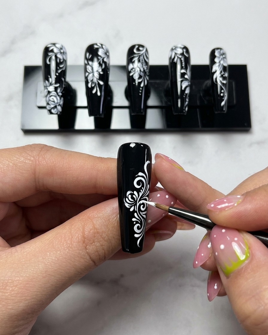 Primo piano di un pennellino che aggiunge linee curve bianche al centro di una rosa su ununghia nera.