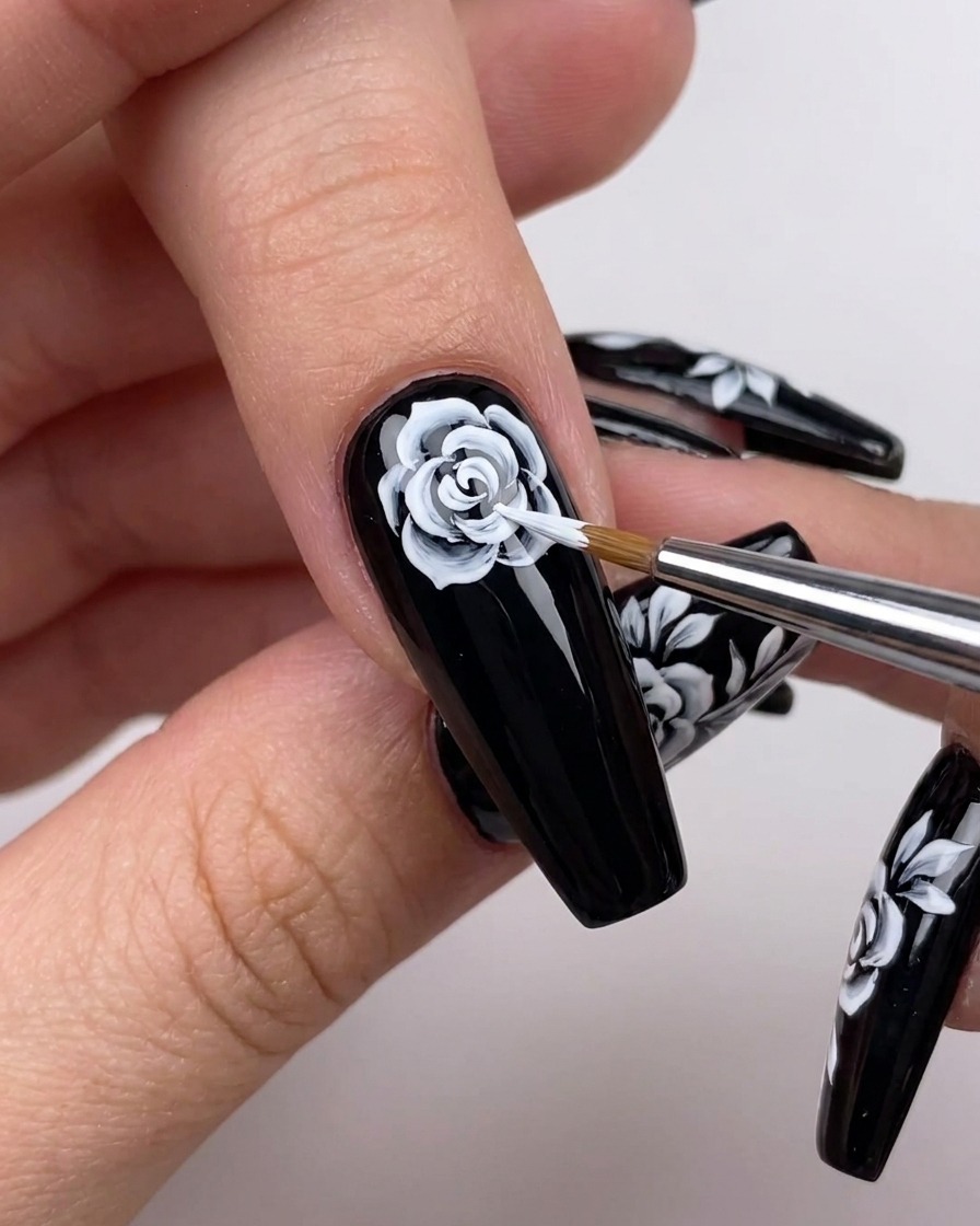 Primo piano di una mano che utilizza un pennello sottile per estendere le linee bianche dei petali verso lesterno in una nail art floreale.