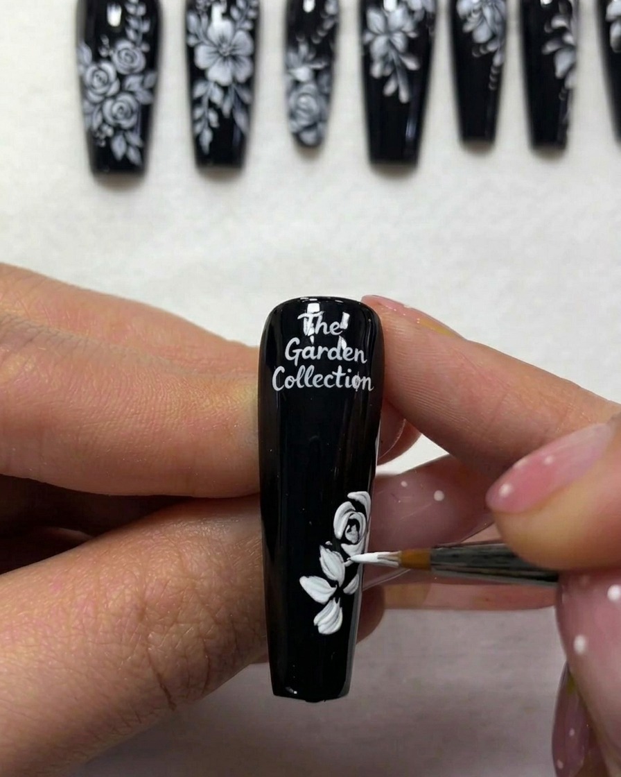Primo piano di una nail artist che aggiunge sottili linee bianche per rappresentare gli steli delle foglie su ununghia dipinta di nero.