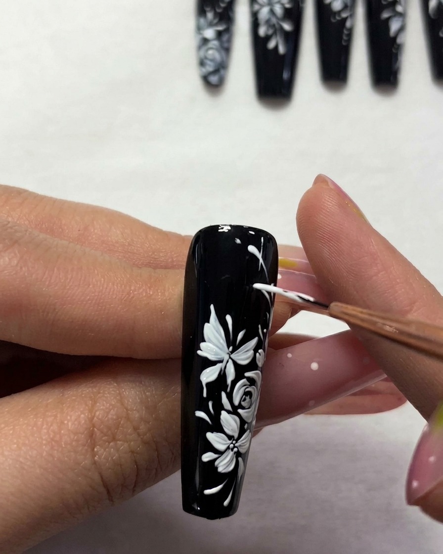 Un pennello applica un top coat trasparente sulla nail art floreale finita.