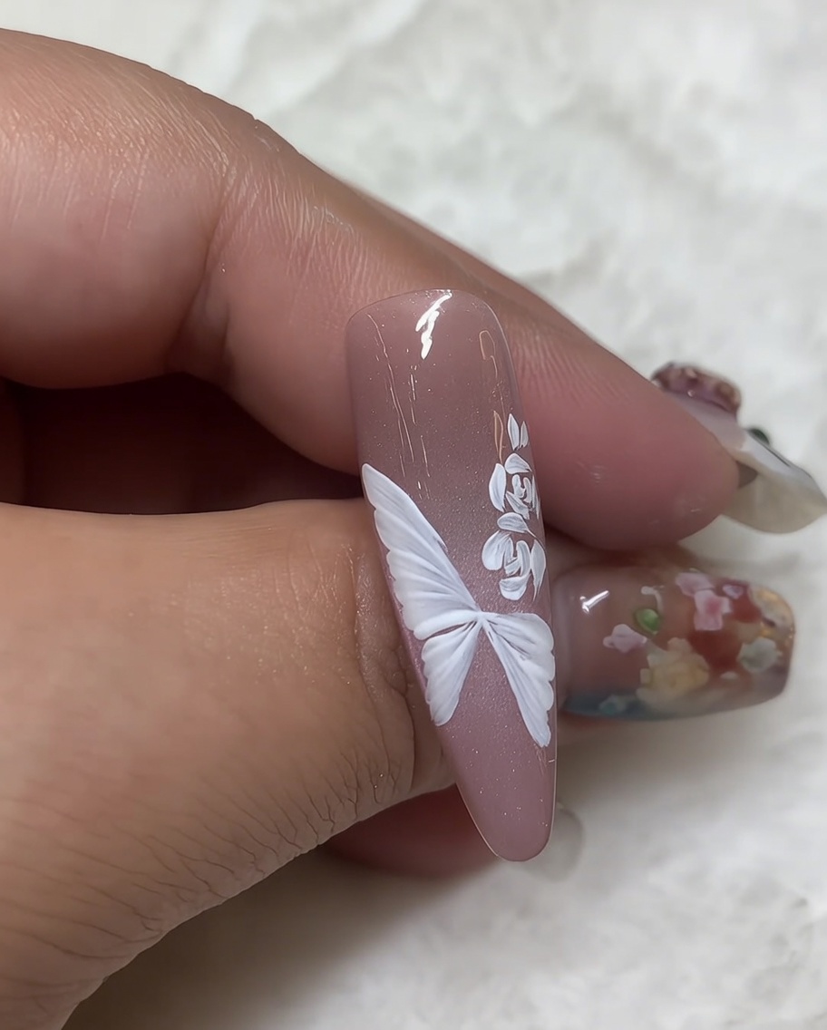 Primo piano di ununghia con una rosa in gel bianco e un pennello liner che aggiunge piccole foglie dettagliate a lato del design floreale.