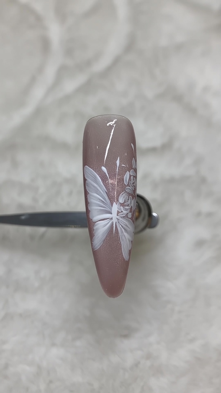 Dettaglio di nail art bianca dipinta a mano con farfalla e rose su una luminosa base cat-eye.