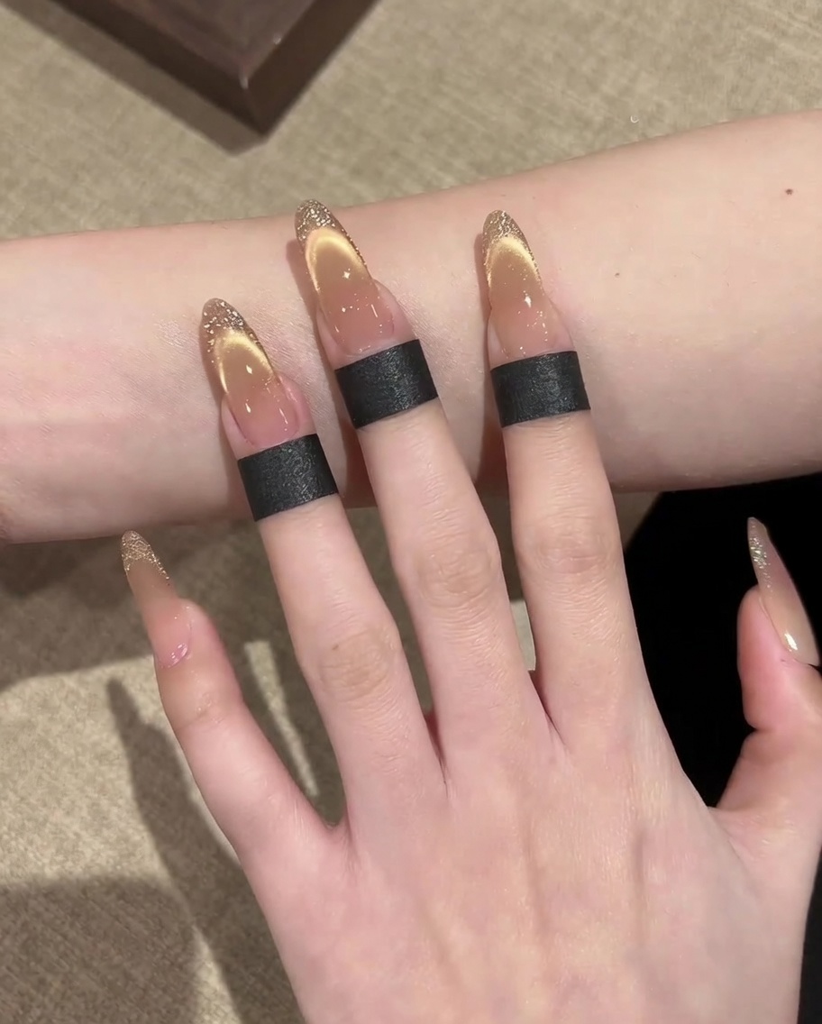 Dettaglio di una mano che usa un pennello liner sottile per disegnare un contorno glitter oro sul bordo della french cat-eye.