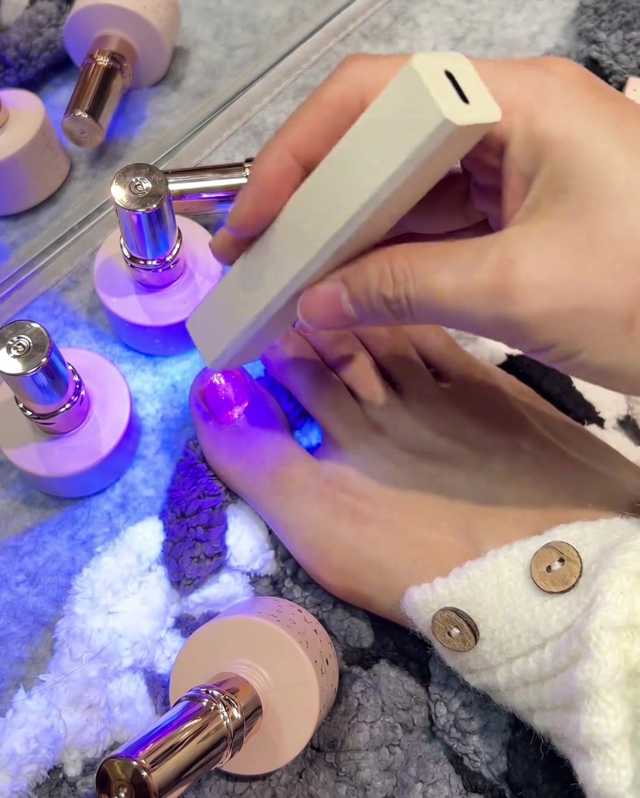 Una mano che utilizza una lampada UV/LED portatile per polimerizzare il gel sullalluce.
