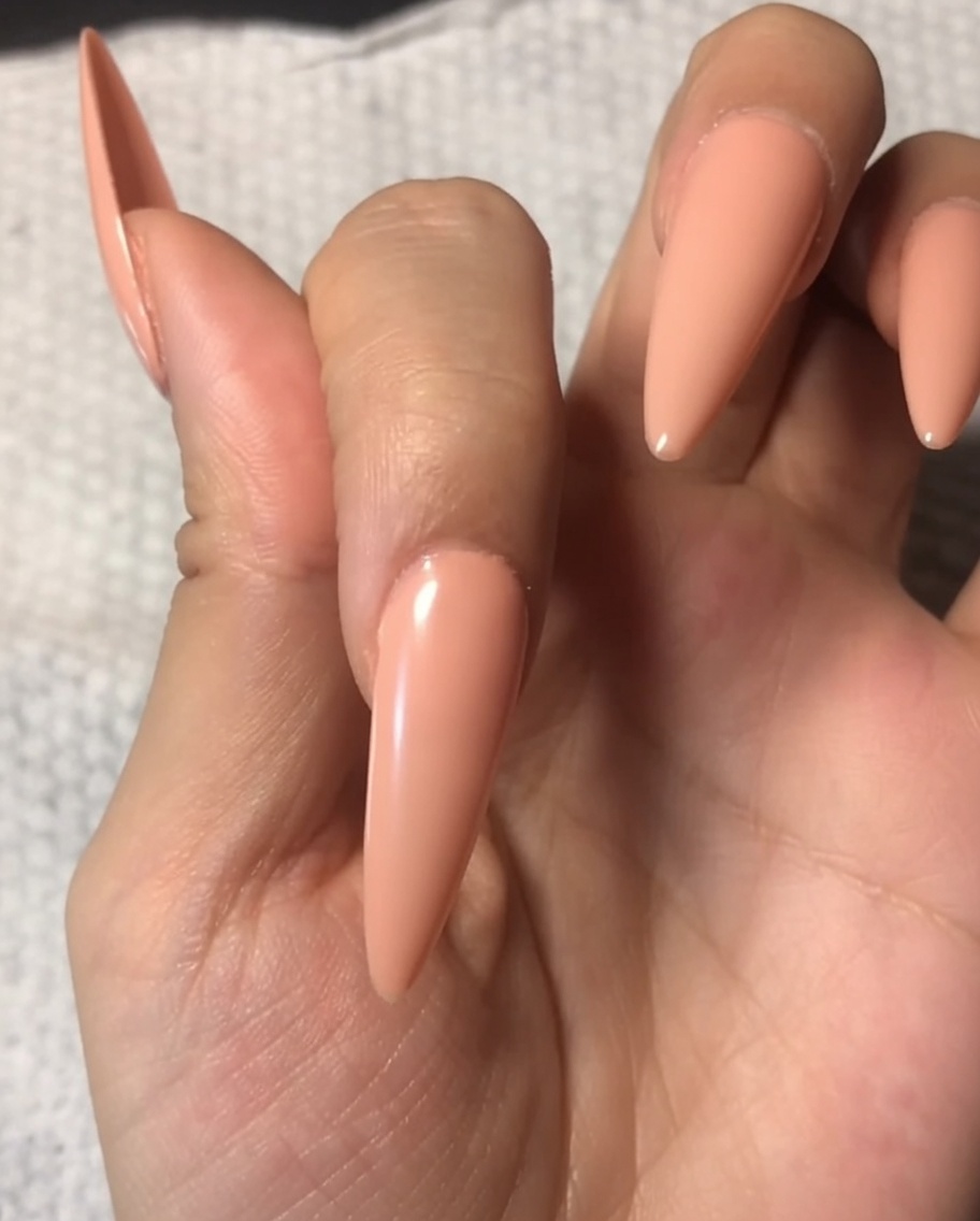 Un pennello che applica un top coat trasparente e lucido su ununghia già dipinta con una base nude delicata.