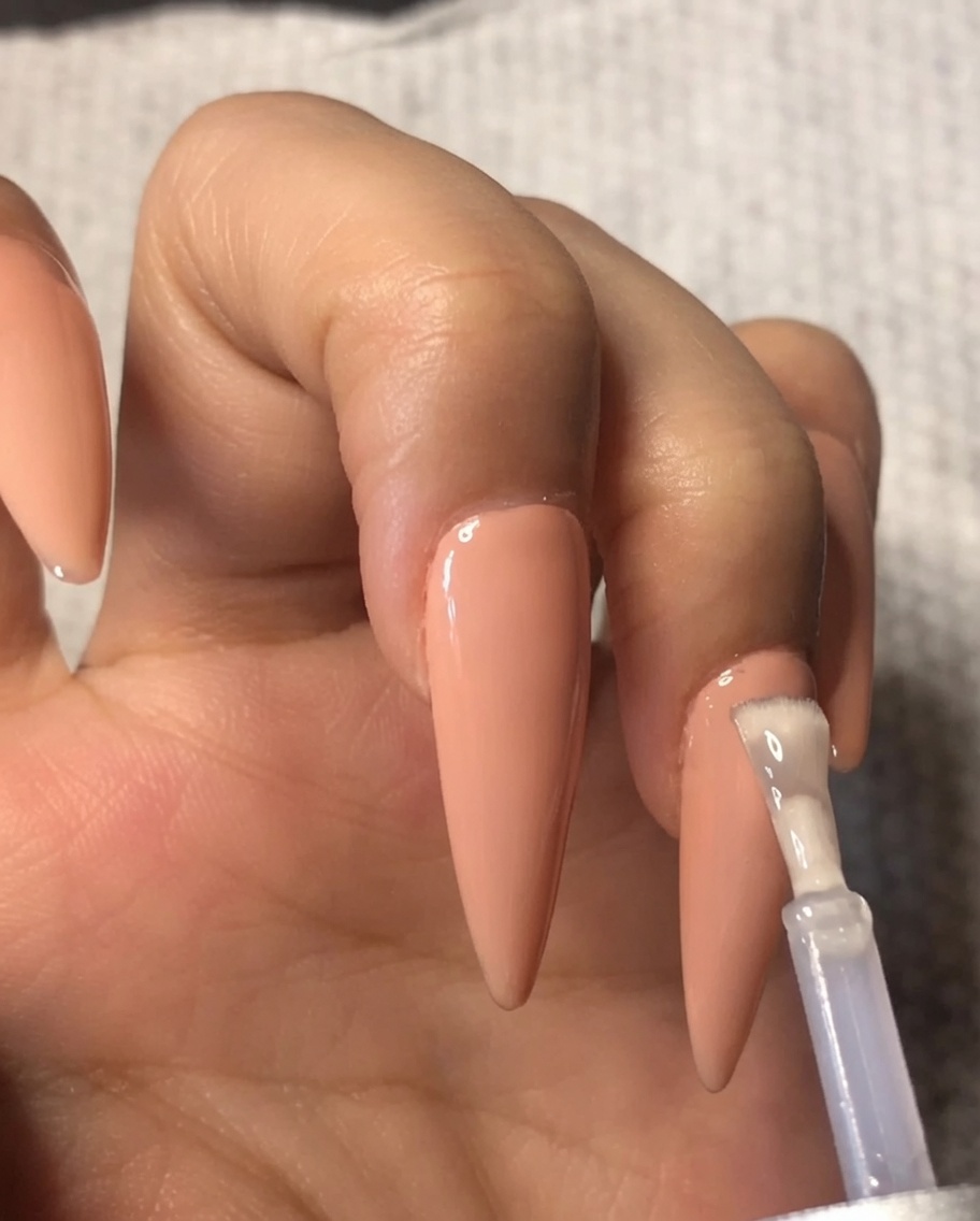 Un pennello che applica uno strato di top coat in gel trasparente su uno smalto nude sullanulare.