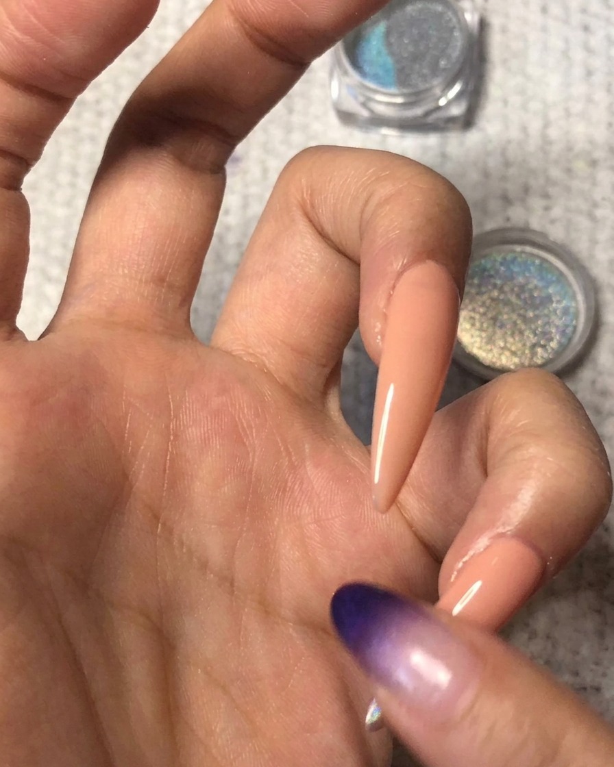 Una punta di dito pulita che sfuma delicatamente il bordo della polvere olografica verso lalto sullunghia nude per creare una sfumatura ombré senza linee nette.